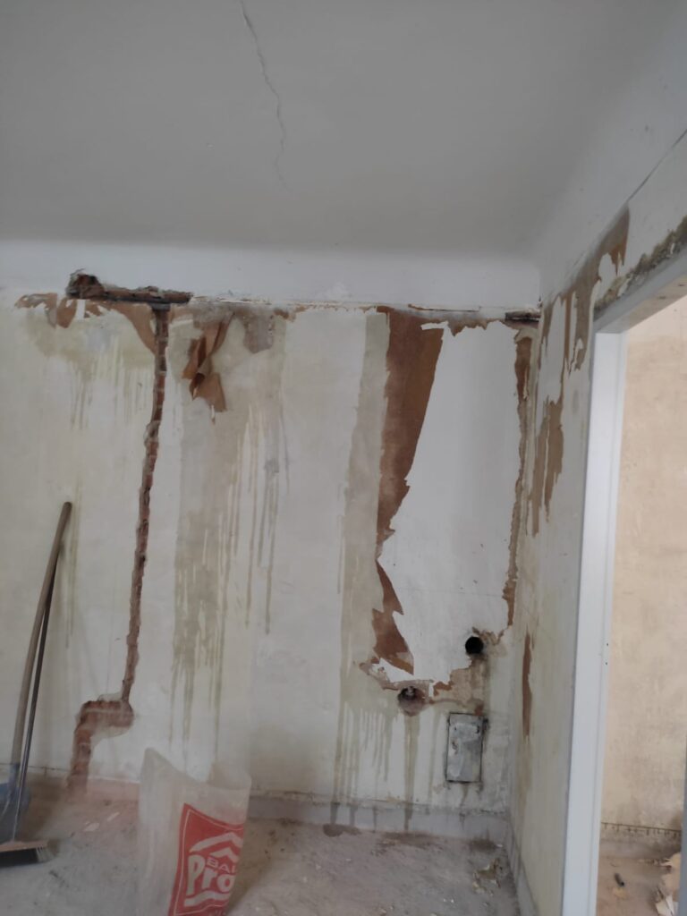 Wand mit Tapetenresten und Schlitzen vor der Sanierung