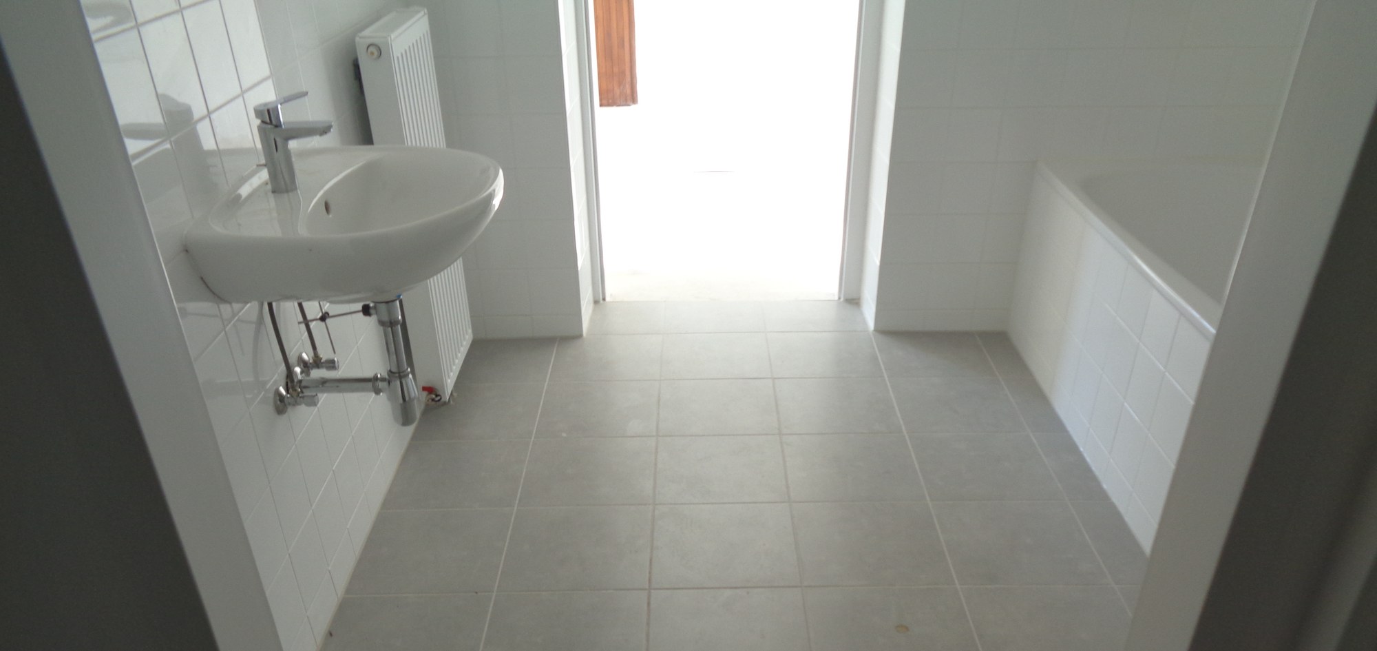 Neues Bad mit Waschbecken, weißen Wandfliesen und Fliesenboden