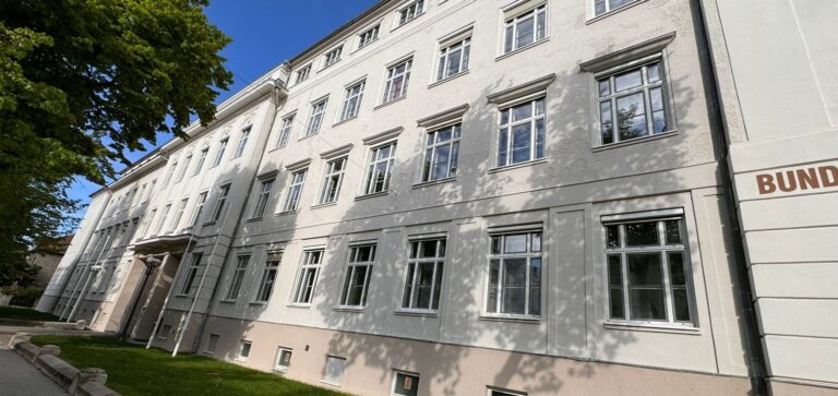 Sanierte Straßenfassade einer Schule in Wiener Neustadt unter blauem Himmel