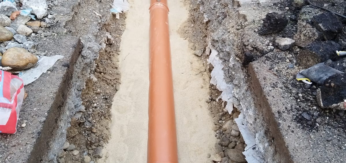 Neu verlegter orangefarbener PVC-Kanal im Sandbett in einem offenen Graben