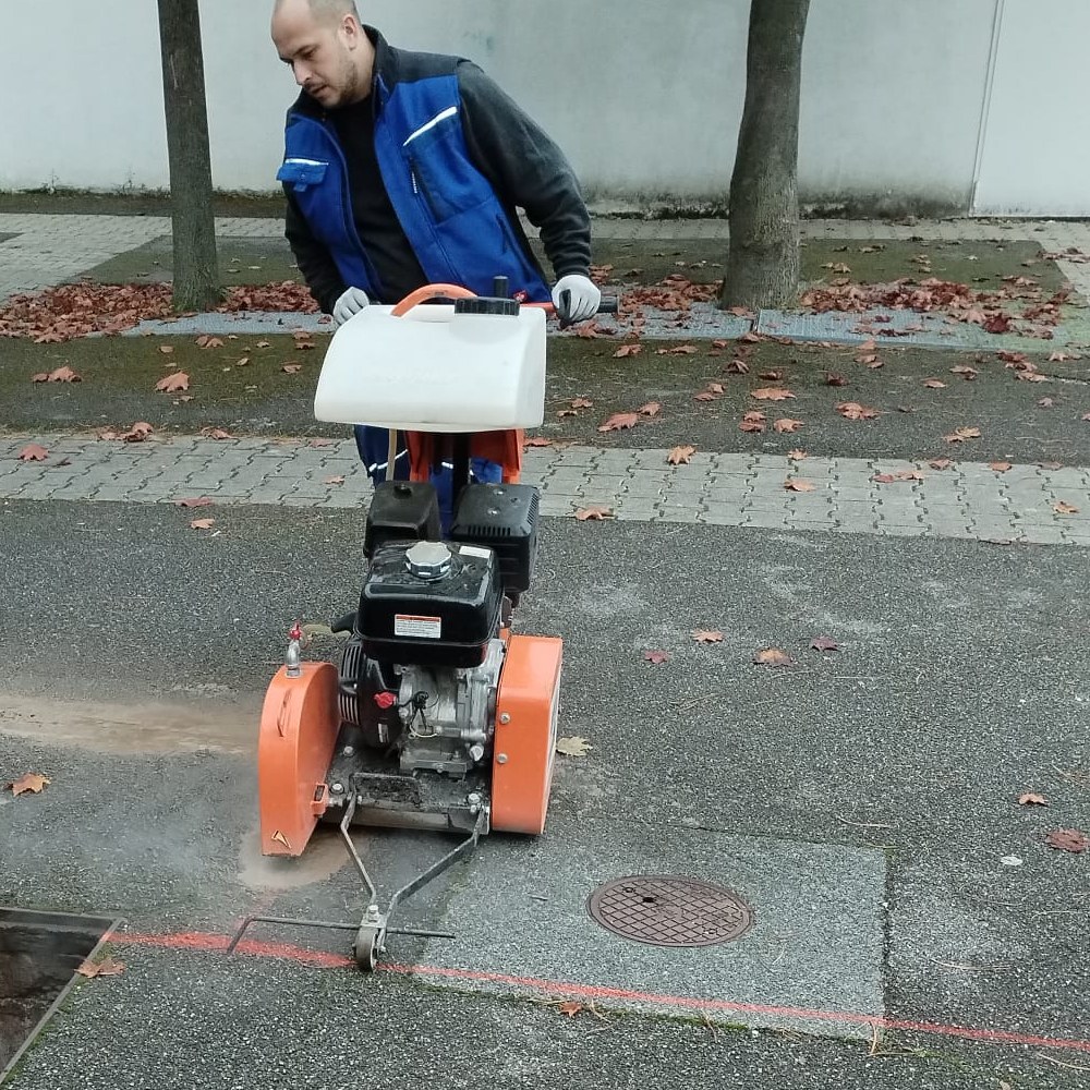 emasan-Mitarbeiter schneidet mit dem Fugenschneider eine Fläche im Hof einer Schule auf