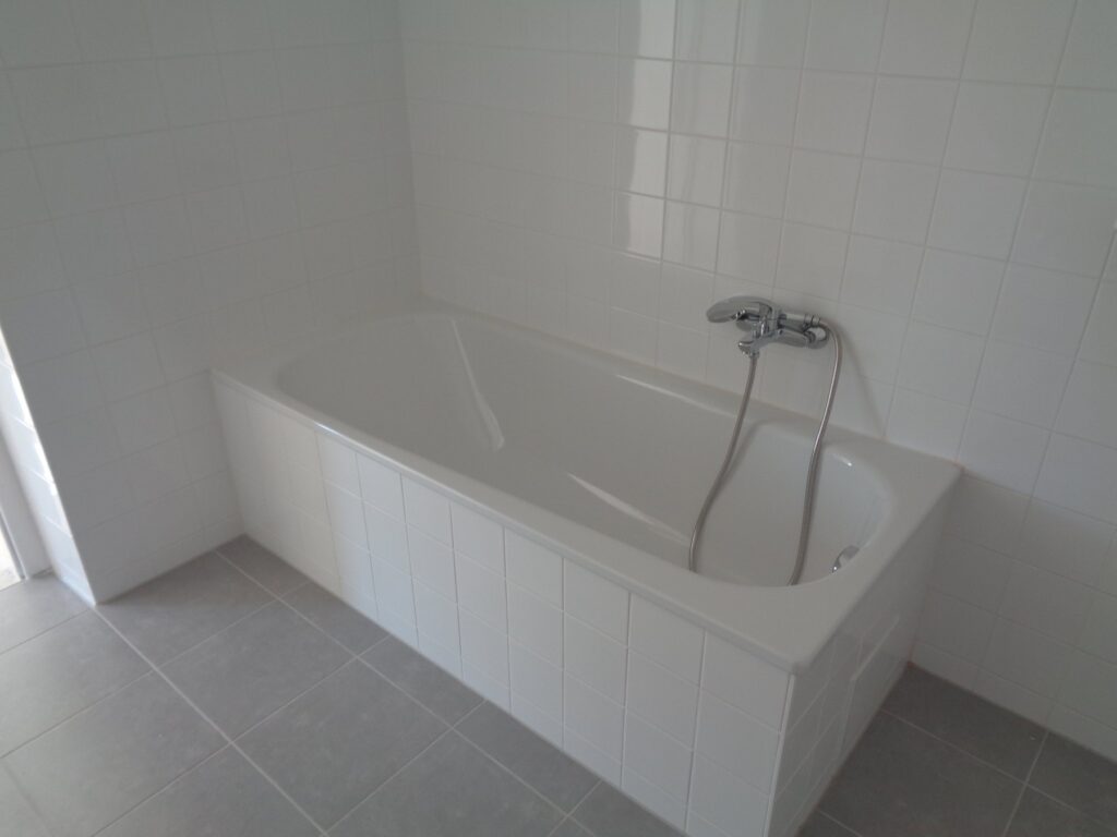 Neues Bad mit weißen Wandfliesen, Badewanne und grauem Fliesenboden