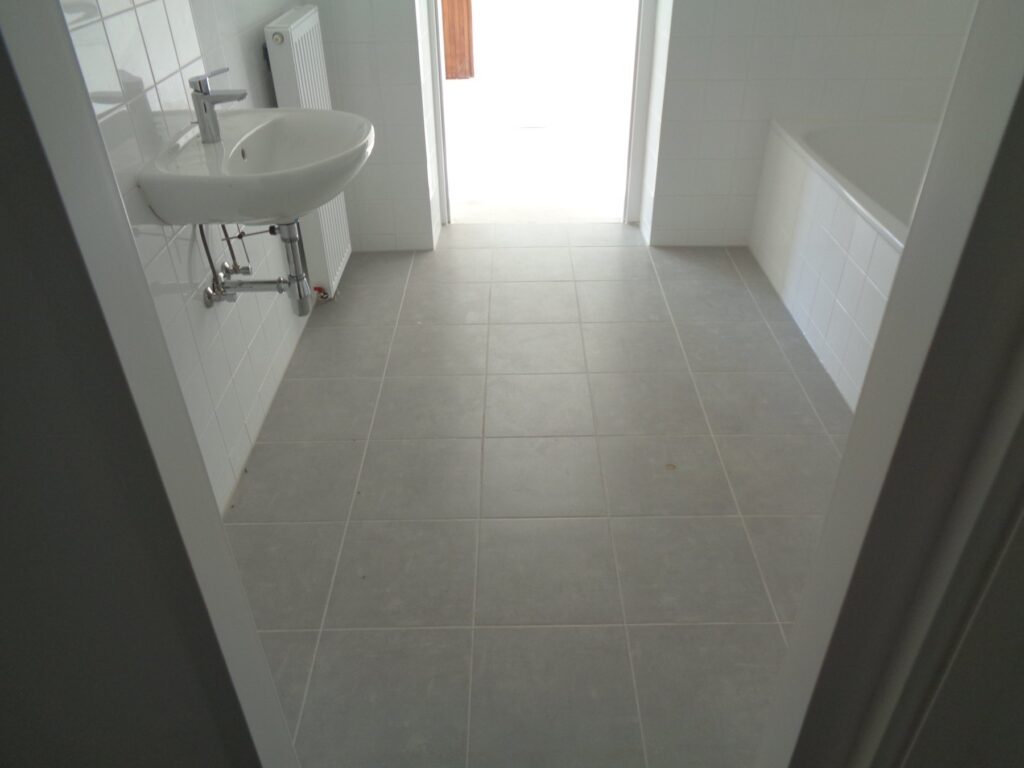 Badezimmer mit Waschbecken, neuem Fliesenboden und Badewanne nach der Sanierung in der Luickgasse