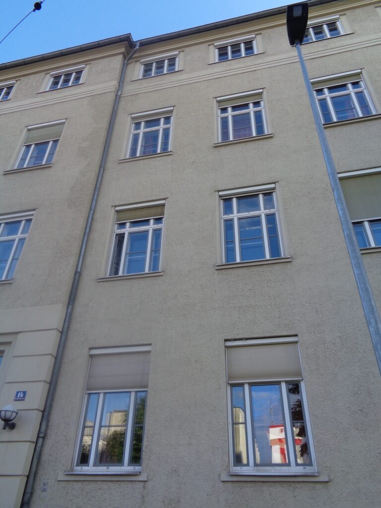 Straßenfassade der Schule vor der Sanierung mit strukturierter Putzfläche und Fensterreihen